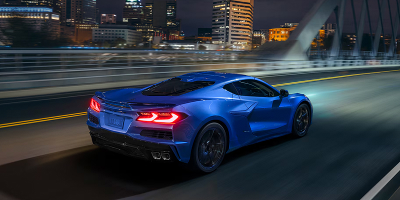 Blue Chevrolet Corvette driving across a bridge at night.